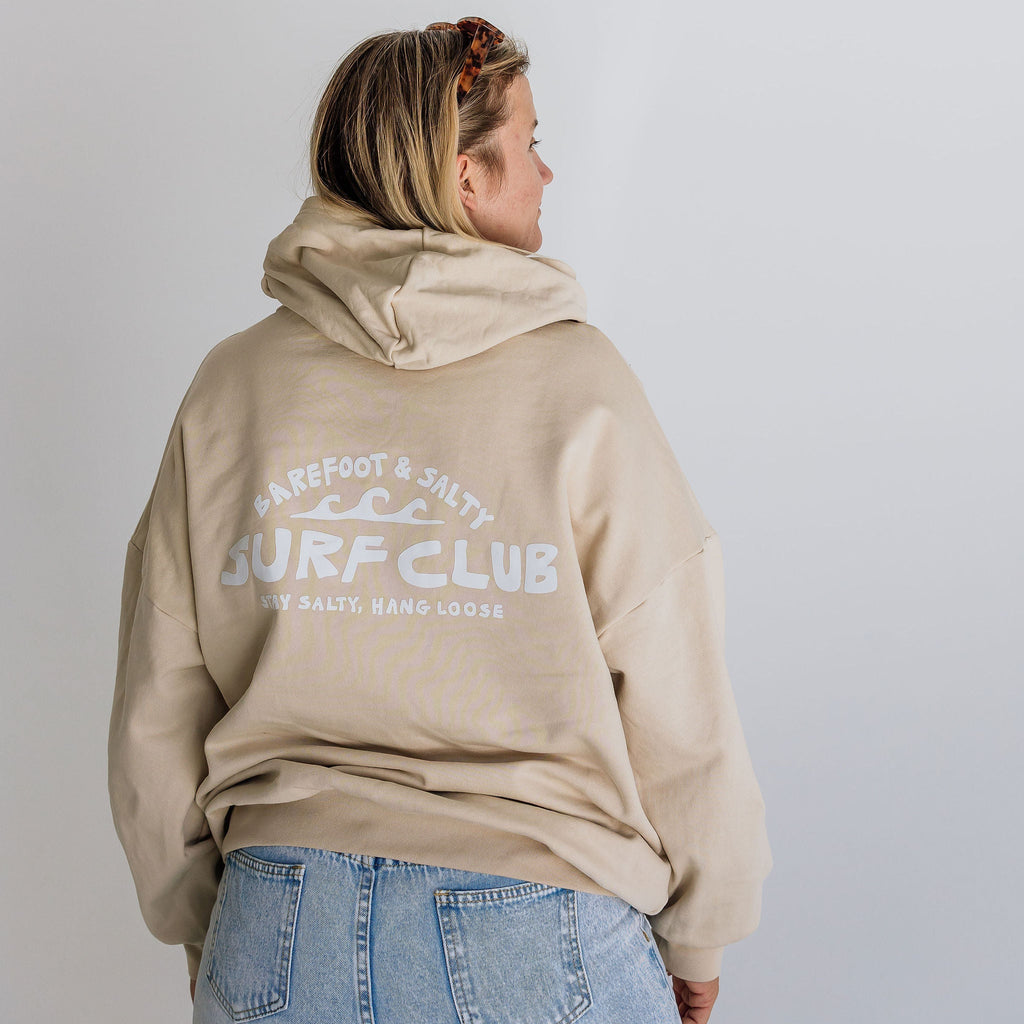 Person wearing a beige hoodie with 'Surf Club' text on the back, standing against a plain background